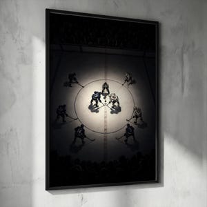 May include: A framed vertical wall art print depicting an overhead view of an ice hockey game face-off. Two players in blue and white jerseys compete for the puck at center ice, surrounded by other players and a referee under a bright spotlight.