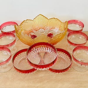 May include: A collection of glassware including a large amber-colored bowl with a scalloped edge, four clear glass footed cups with red rims, and three clear glass bowls featuring a textured diamond pattern and red-tinted edges.