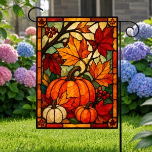 May include: A rectangular garden flag featuring a stained glass style design of three pumpkins and autumn maple leaves in shades of orange, red, and yellow. The artwork includes small red berries on branches and a dark border with leaf motifs.