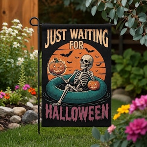 May include: A black rectangular garden flag featuring a skeleton lounging in a teal inflatable pool ring. The skeleton holds a jack-o'-lantern against an orange moon background with bats. The text reads JUST WAITING FOR HALLOWEEN in bold letters.