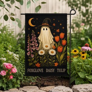 May include: A rectangular garden flag with a black background featuring a central white ghost wearing a witch hat, surrounded by illustrations of purple foxgloves, white daisies, and orange tulips, with a yellow crescent moon and the text FOXGLOVE DAISY TULIP.