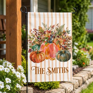 May include: A rectangular garden flag featuring a vertical beige and white striped background. The center displays a watercolor illustration of orange and green pumpkins surrounded by autumn leaves, berries, and ferns. The text reads The Smiths.
