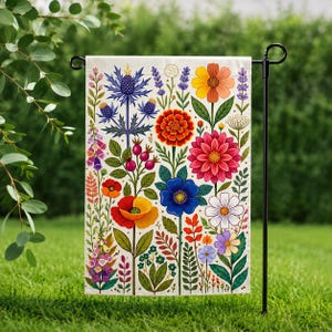 May include: A garden flag featuring a vibrant floral design. The flag showcases a variety of colorful flowers, including red poppies, blue thistle, and yellow daisies, set against a cream background. The flag is displayed on a black metal stand, perfect for outdoor decor.