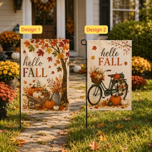 May include: Two rectangular garden flags on metal stands. Design 1 features a tree, pumpkins in a wooden cart, and the text 'hello FALL'. Design 2 shows a bicycle with a basket of pumpkins, a plaid blanket, and the text 'hello FALL'.