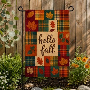 May include: A rectangular garden flag featuring a patchwork design of plaid squares in shades of red, orange, green, and yellow. The center panel is beige with the text hello fall in dark brown script, surrounded by various autumn leaf illustrations.