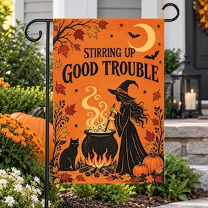 May include: A rectangular orange garden flag featuring a witch stirring a black cauldron over a fire, a black cat, pumpkins, and autumn leaves. The text reads STIRRING UP GOOD TROUBLE in black letters, with a yellow crescent moon and bats above.
