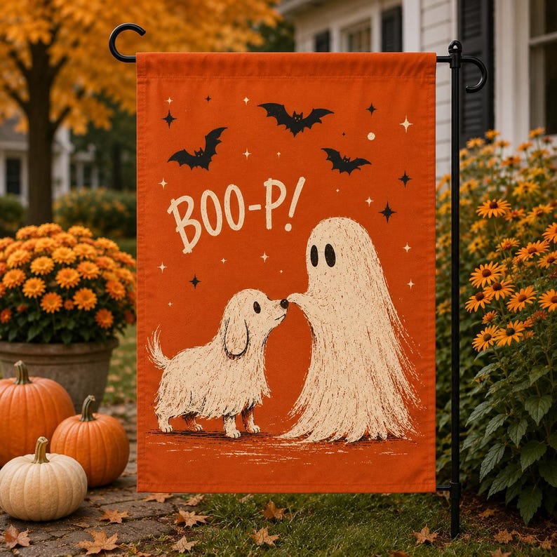 May include: A rectangular orange garden flag featuring a white illustration of a small dog and a ghost touching noses. The text BOO-P! is printed in white above the figures, accompanied by black bat silhouettes and small white star accents.