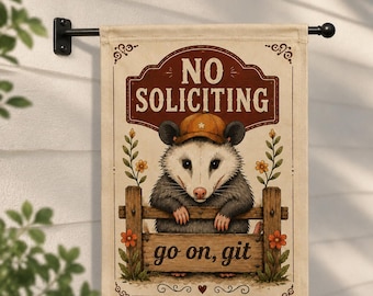 May include: A rectangular garden flag featuring a cream background with a brown border. It displays an illustration of an opossum wearing a tan baseball cap, leaning on a wooden fence. The text reads NO SOLICITING at the top and go on, git below.