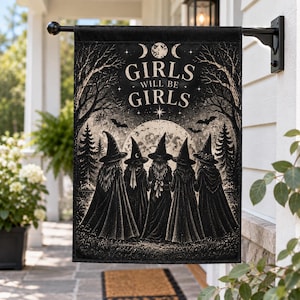 May include: A rectangular black and white garden flag featuring five figures in pointed hats and cloaks standing before a large full moon. The text GIRLS WILL BE GIRLS is printed in the center above the figures, with trees and bats in the background.