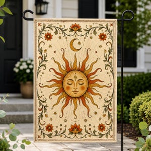 May include: A rectangular garden flag featuring a central sun with a human face and closed eyes, surrounded by radiating orange and yellow rays. Above the sun is a crescent moon and star. The border displays orange flowers and green vines.