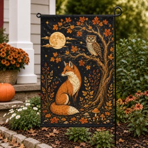 May include: A rectangular garden flag featuring a black background with a central orange fox sitting beneath a tree. An owl is perched on a branch, and a large full moon shines above. The scene includes orange autumn leaves, small mushrooms, and stars.