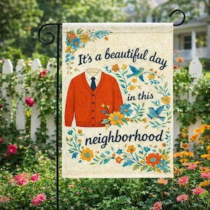 May include: A rectangular garden flag with a beige linen-like texture featuring an orange button-down cardigan, blue birds, and colorful floral accents. The text reads, "It's a beautiful day in this neighborhood," in dark blue script.