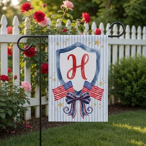 May include: A patriotic garden flag featuring a blue and white striped background with a shield design. The shield contains a red letter "H", two American flags, and a blue bow. Gold stars are scattered around the design.