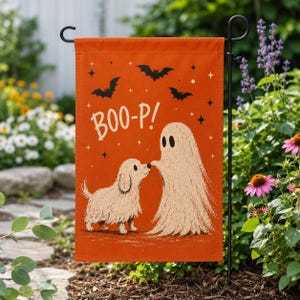 May include: A rectangular orange garden flag featuring a cream-colored illustration of a small shaggy dog and a ghost touching noses. The text BOO-P! is printed in white above the figures, surrounded by small black bats and star accents.