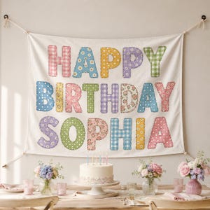 May include: A rectangular fabric wall hanging featuring the text HAPPY BIRTHDAY SOPHIA in large, multi-colored, patterned letters. Each letter displays a unique design, including gingham, polka dots, and floral prints in pastel shades.