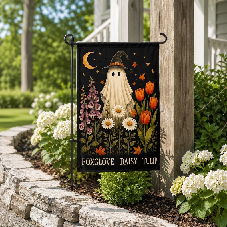 May include: A black garden flag featuring a central white ghost wearing a witch hat, surrounded by orange tulips, white daisies, and purple foxgloves under a crescent moon and stars. The text FOXGLOVE DAISY TULIP is printed at the bottom.