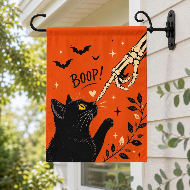 May include: A rectangular orange garden flag featuring a black cat with yellow eyes reaching up to touch a skeletal finger. The text BOOP is printed in black above the cat. The design includes black bats, white stars, and a black leafy vine.