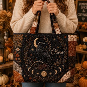 May include: A quilted tote bag featuring a black raven perched on a branch under a crescent moon, surrounded by a lunar cycle and floral motifs. The name Olivia is embroidered in script. The bag has a patchwork design with autumn-toned fabrics.
