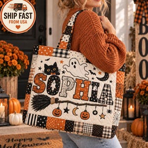 May include: A quilted tote bag featuring the name SOPHIA in large orange and black letters. The design includes a black cat, a white ghost, a broomstick, pumpkins, stars, and spiderwebs on a cream background with black and orange borders.