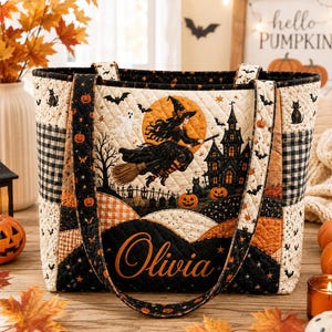 May include: A quilted tote bag featuring a Halloween scene with a witch flying on a broomstick, a haunted house, bats, ghosts, and pumpkins. The bag has a black and orange color palette with a cream background and the name Olivia embroidered in gold.