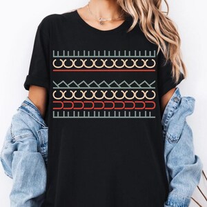 May include: Black t-shirt with a colorful geometric pattern. The design includes rows of interlocking circles, zigzags, and vertical lines in red, yellow, blue, and green. The shirt is a casual wear item.