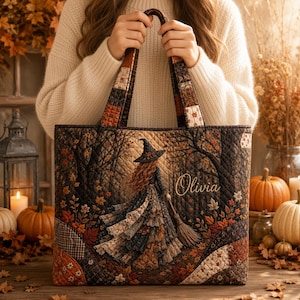 May include: A quilted tote bag featuring a fall-themed design with a witch holding a broomstick, surrounded by autumn leaves and trees. The name Olivia is embroidered in script on the front. The bag has a patchwork pattern on the handles.
