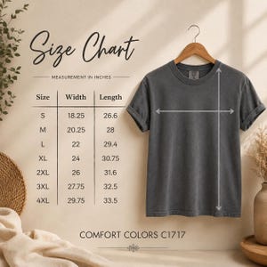 May include: A charcoal grey short-sleeve t-shirt hanging on a wooden hanger, accompanied by a size chart with measurements in inches. The chart lists sizes S through 4XL with corresponding width and length dimensions. Text reads Comfort Colors C1717.