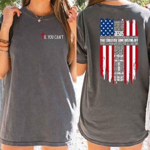 May include: Dark gray t-shirt with a red cross and the text "IL YOU CAN'T" on the front. The back features a distressed American flag design with religious text, including "JESUS".