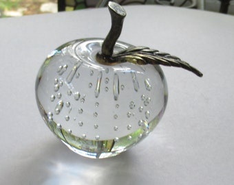Könnte beinhalten: Ein durchsichtiger Glasapfel-Briefbeschwerer mit einem silbernen Stiel und Blatt. Der Apfel ist mit kleinen Luftblasen gefüllt.