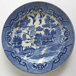 Puede incluir: Un plato de porcelana azul y blanco con un diseño chino tradicional. El plato presenta una imagen central de una pagoda, un puente y un sauce llorón, todo rodeado por un borde decorativo.