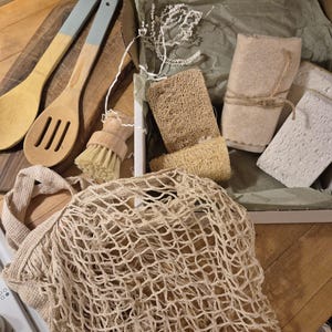 May include: A kitchen set containing a beige cotton mesh market bag, two wooden spoons with light blue handles, a small round wooden scrubbing brush, two textured loofah sponges, and two white rectangular sponges inside a cardboard box.