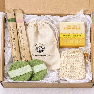 May include: A box containing sustainable personal care products. It features bamboo toothbrushes, facial puffs, a soap bar, a drawstring bag, and a soap saver. The soap bar is yellow and labelled "HAND SOAP BAR".