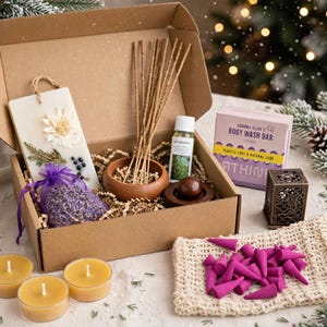 Peut inclure: Une boîte cadeau en carton contenant une tablette de cire blanche avec des fleurs séchées, un sachet en organza violet de lavande, un bol en bois avec des bâtonnets d'encens, une huile de romarin, un savon solide, un brûle-encens et des cônes roses.