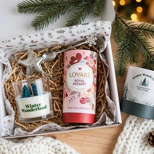 以下が含まれることがあります： 青い木型のワックスが入ったガラスキャンドル、Lovare Royal Dessertティーの円筒形容器、銀色の星型ティーインフューザーが入ったギフトボックス。箱の横には、森のグラフィックが描かれたWinter Wonderlandキャンドルが置かれています。