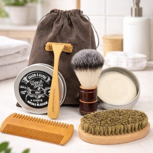 Op de afbeelding: Een verzorgingsset met een houten scheermes, scheerkwast, kam en een ronde borstel. De set bevat een blik scheerzeep met tekst, een stuk zeep en een zakje met trekkoord. De items zijn gerangschikt op een wit oppervlak.