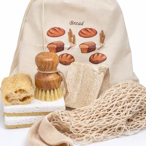 May include: A beige drawstring bread bag with a printed graphic of loaves and wheat, accompanied by a wooden dish brush, two rectangular white sponges, a textured loofah piece, and a beige mesh produce bag for kitchen organization.