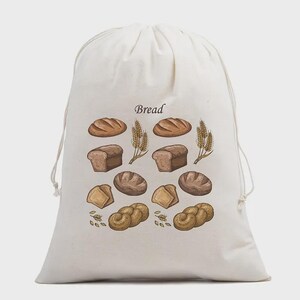 May include: An off-white drawstring bag featuring a printed graphic of various types of bread and wheat stalks. The word Bread is printed in a dark font above the illustrations. The bag is made of a light-colored fabric and has two drawstrings.