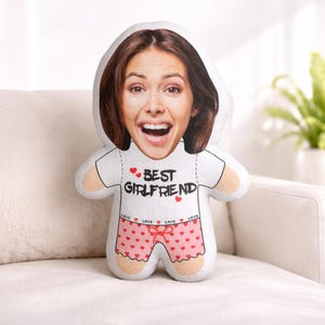 Peut inclure: Une poupée en peluche avec le visage d'une femme, portant un t-shirt blanc avec "BEST GIRLFRIEND" imprimé et un short rose à motifs de cœurs. La poupée est conçue pour ressembler à une personne.