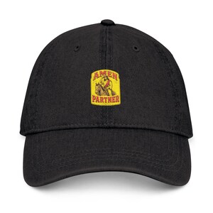 May include: Black baseball cap with a curved brim. The cap features a rectangular patch with the words "AMEN PARTNER" and an illustration of a person riding a horse. The patch has a yellow background with red and brown accents.