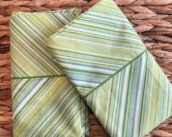 May include: Two folded pillowcases featuring a diagonal striped pattern in shades of lime green, light blue, and white. The fabric displays a consistent linear design across the surface, with a prominent dark green horizontal seam line.