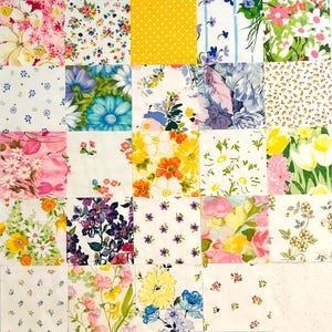 May include: A patchwork quilt top composed of twenty-four square fabric blocks featuring a variety of floral, botanical, and geometric patterns in shades of yellow, pink, blue, green, and white, arranged in a grid formation on a flat surface.