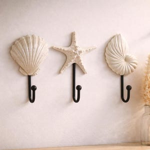 Peut inclure: Ensemble de trois mugs en céramique avec une finition mate et mouchetée. Les tasses sont de couleur crème, gris clair et gris foncé. Chaque mug a un design simple et minimaliste avec une anse arrondie.