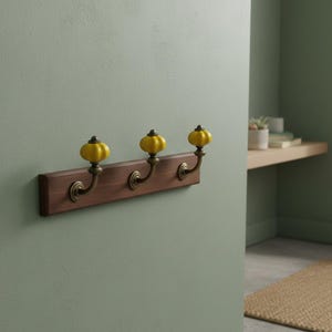 Perchero de pared vintage con ganchos dorados y pomos de cerámica amarilla para la decoración de la entrada.
