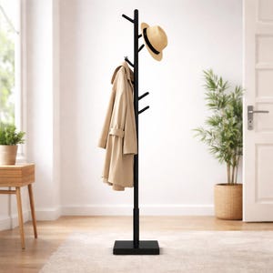 May include: A black coat stand with multiple hooks, holding a beige trench coat and a straw hat. The coat stand is in a room with a neutral colour scheme. The stand has a square base and a tree-like design.