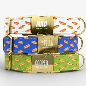 May include: Three personalized dog collars with gold-colored buckles. The collars feature a repeating pattern of hot dogs on white, blue, and green backgrounds. Each buckle is engraved with a name and phone number.
