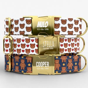 May include: Three personalized dog collars with gold-colored buckles. The top collar has a white background with brown teddy bears, the middle one has a white background with brown teddy bears and red hearts, and the bottom one has a navy blue background with brown teddy bears and yellow stars. Each collar has a name and phone number.