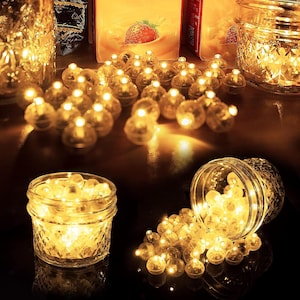 May include: A collection of warm, glowing fairy lights in small, clear, round bulbs are displayed in and around glass jars. The lights are scattered on a dark surface, creating a cosy, inviting ambience. The jars have textured and smooth surfaces.