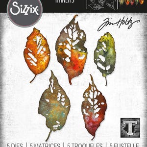 May include: A set of five leaf-shaped Thinlits dies by Sizzix, designed by Jim Holtz. The dies feature intricate, distressed leaf designs in shades of orange, brown, and green. The packaging includes the Sizzix logo and product information.