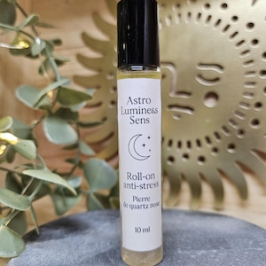 Puede incluir: Un frasco roll-on de vidrio transparente con tapa negra. La etiqueta dice "Astro Luminess Sens" y "Roll-on anti-stress". El frasco contiene un líquido amarillo claro y está etiquetado como "Pierre de quartz rose" y "10 ml".