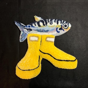 Könnte beinhalten: Ein skurriles Teppichdesign mit einem Fisch mit blau-weißen Streifen über einem Paar gelber Gummistiefel. Die Stiefel haben schwarze Verzierungen und weiße Details. Der Hintergrund ist einfarbig schwarz.
